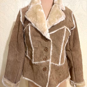 May include: Brown suede jacket with a cream-colored faux fur collar and trim. The jacket features a button-up front and decorative stitching. The jacket is displayed on a mannequin.
