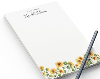 May include: A white notepad with a sunflower border and the text "A note from Meredith Robinson" at the top. A black pencil is lying on top of the notepad.