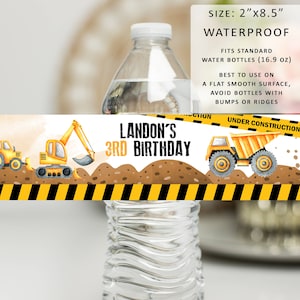 May include: Water bottle label with a construction theme. It features a yellow excavator and dump truck on a brown dirt background with a yellow and black striped border. The text "LANDON'S 3RD BIRTHDAY" is in black letters. The label is 2 inches by 8.5 inches and is waterproof.