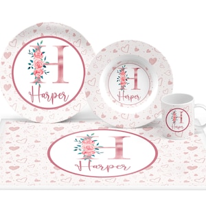 May include: A pink and white personalized children's dinnerware set with a floral design and the name "Harper". The set includes a large plate, a smaller bowl, and a mug.