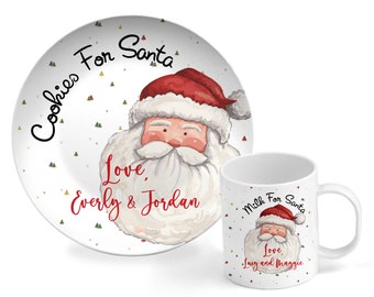 Könnte beinhalten: Ein weißer Keramikteller mit einer rot-weißen Illustration des Weihnachtsmanns. Der Teller trägt den Text "Cookies For Santa" und "Love, Everly & Jordan". Eine weiße Keramiktasse mit einer rot-weißen Illustration des Weihnachtsmanns. Die Tasse trägt den Text "Milk For Santa" und "Love, Lucy and Maggie".