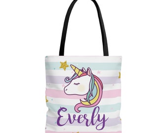 May include: A white tote bag with a pink, blue, and purple striped pattern. The bag features a cartoon unicorn with a gold horn and a gold star above it. The word "Everly" is printed in purple on the bag.