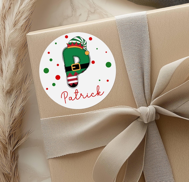 May include: A round sticker with the name "Patrick" in red script. The letter "P" is designed as an elf with a green hat and outfit. Red and green dots surround the sticker, which is placed on a gift box with a ribbon.