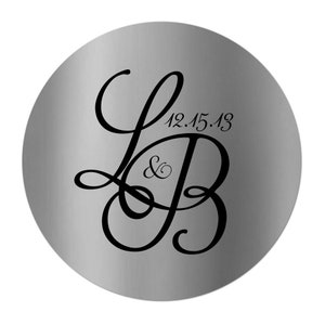 May include: A round, silver-colored object with a brushed metal finish. The design features the intertwined letters "L" and "B" in a flowing script, with the date "12.15.13" above. The ampersand symbol is between the letters.