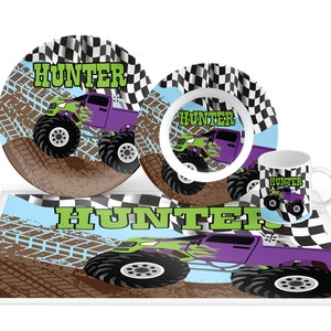 May include: A four-piece monster truck themed children's dinnerware set with a plate, bowl, cup, and placemat. The set features a green and purple monster truck with flames and the name "Hunter" on each piece. The background is a checkered flag pattern with a dirt track design.