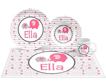 May include: A pink and gray children's dinnerware set with a pink elephant design and the name "Ella" on each piece. The set includes a plate, bowl, and cup.