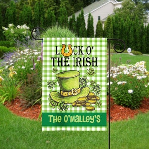 May include: A green and white checkered garden flag with the text "Luck o' the Irish" and a cartoon illustration of a green leprechaun hat with a gold buckle and gold coins. The flag also includes the text "The O'Malley's".