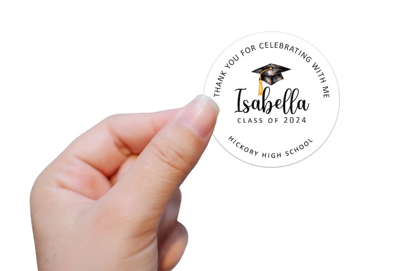 May include: Round white sticker with black text that says "Thank you for celebrating with me Isabella Class of 2024 Hickory High School". A black graduation cap with a gold tassel is above the text.