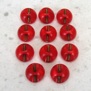 May include: Nine bright red buttons with a gold-colored vertical accent. The buttons are round with a slightly domed shape and a recessed area on either side of the gold accent. The buttons are arranged in a grid pattern.