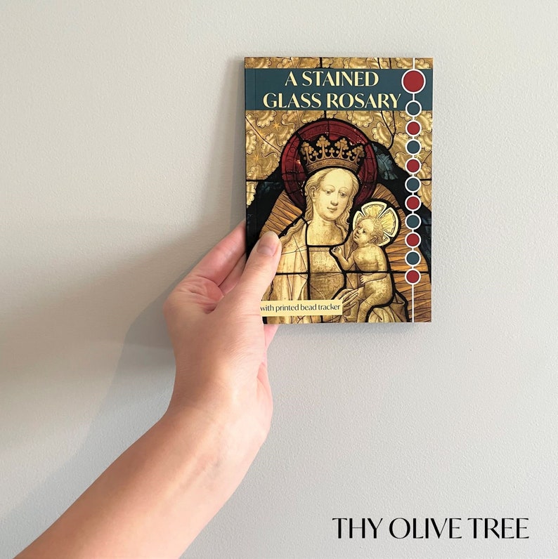 May include: A stained glass rosary with a printed bead tracker. The image shows the Virgin Mary holding baby Jesus. The book cover reads "A Stained Glass Rosary" and "Thy Olive Tree".