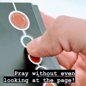 May include: A black card with white circles and red circles. The text "Pray without even looking at the page!" is printed on the card.
