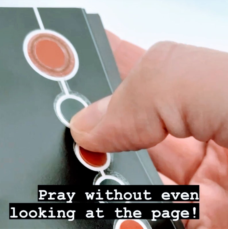 May include: A black card with white circles and red circles. The text "Pray without even looking at the page!" is printed on the card.