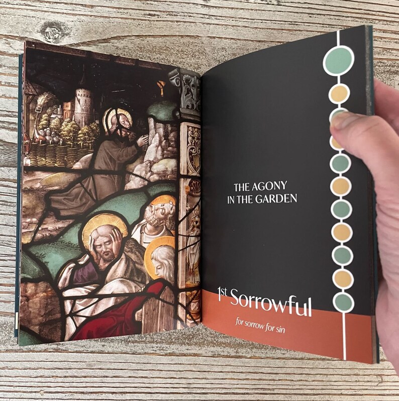 May include: An open book with a stained glass image of Jesus praying in the garden of Gethsemane. The text on the right page reads "The Agony in the Garden" and "1st Sorrowful for sorrow for sin".