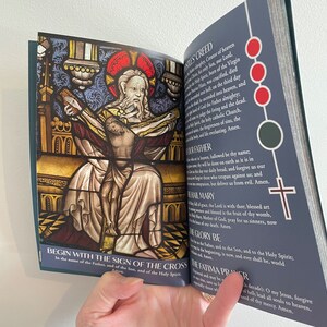 May include: An open book with a stained glass image of Jesus on the cross. The book contains a prayer guide with the words "Begin with the sign of the cross" and "Fatima Prayer".