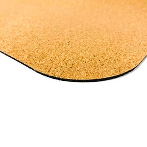 May include: A tan-colored cork mat with a textured, granular surface and a rounded corner. The underside of the mat features a thin, solid black layer, providing a distinct contrast to the natural light brown cork material visible on the top side.