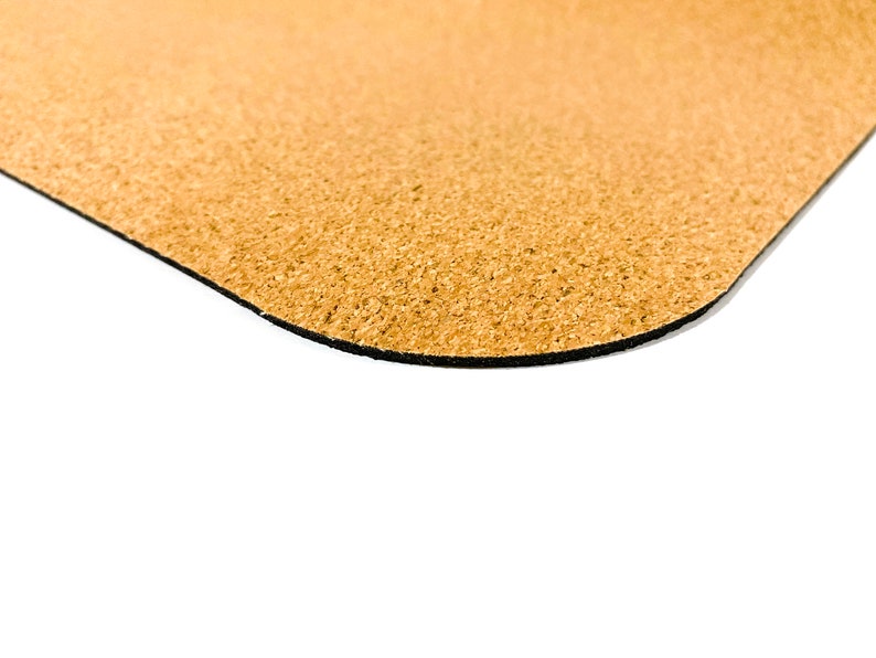 May include: A tan-colored cork mat with a textured, granular surface and a rounded corner. The underside of the mat features a thin, solid black layer, providing a distinct contrast to the natural light brown cork material visible on the top side.