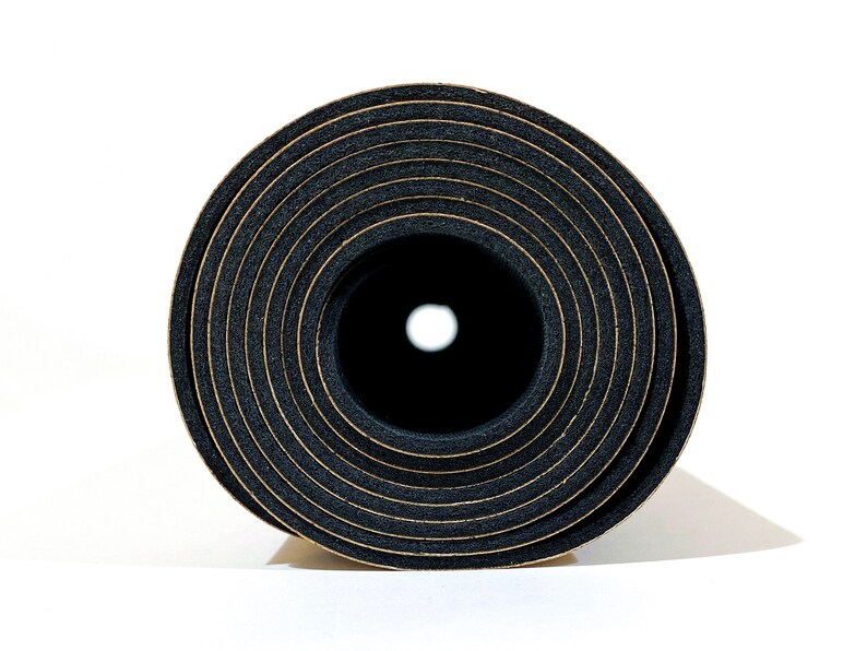 May include: A tightly rolled black foam mat viewed from the end, revealing a circular cross-section with concentric rings. The material has a porous, textured appearance with thin, light-colored lines separating each layer of the rolled foam.