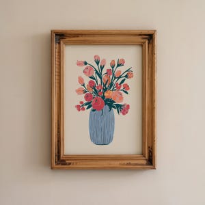 Pode incluir: Uma impressão artística emoldurada com uma ilustração estilizada de um buquê de flores rosas, coral e vermelhas com folhas verde-escuras, dispostas num vaso azul-claro com riscas verticais. A obra está numa moldura de madeira rústica.