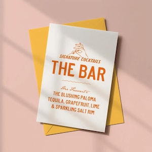 May include: A white card with orange text and a yellow envelope. The card reads "SIGNATURE COCKTAILS THE BAR" and lists ingredients for "THE BLUSHING PALOMA" cocktail: tequila, grapefruit, lime, and sparkling salt rim.