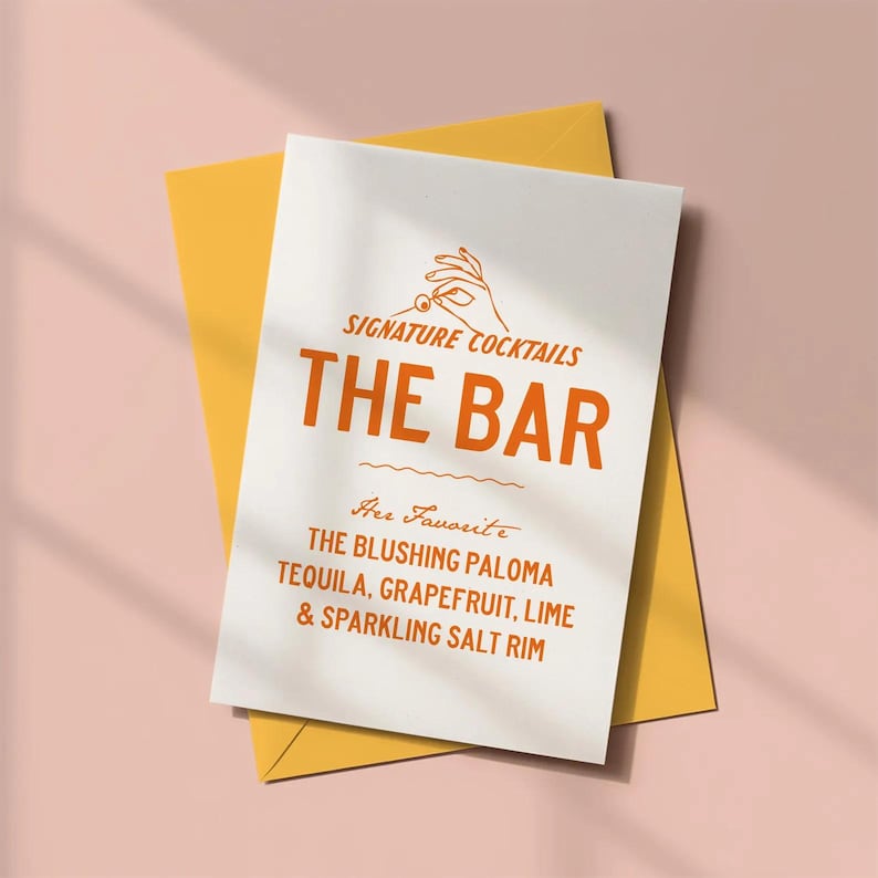 May include: A white card with orange text and a yellow envelope. The card reads "SIGNATURE COCKTAILS THE BAR" and lists ingredients for "THE BLUSHING PALOMA" cocktail: tequila, grapefruit, lime, and sparkling salt rim.