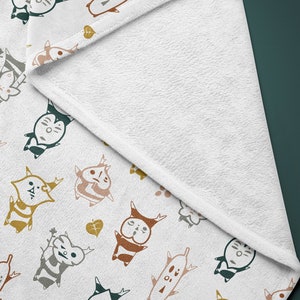 May include: White fleece blanket with a repeating pattern of colorful cartoon characters with antlers and leaves. The characters are in various poses and have different facial expressions.