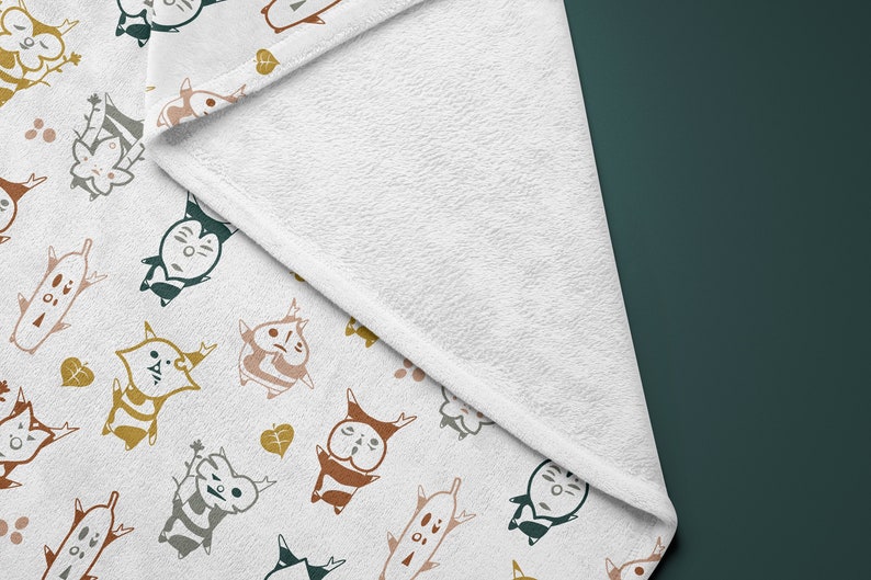 May include: White fleece blanket with a repeating pattern of colorful cartoon characters with antlers and leaves. The characters are in various poses and have different facial expressions.