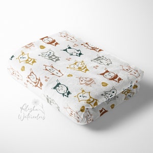 May include: A white fabric baby blanket with a repeating pattern of colorful cartoon cats. The cats are in various poses and have different facial expressions. The background is white with small brown and green dots.