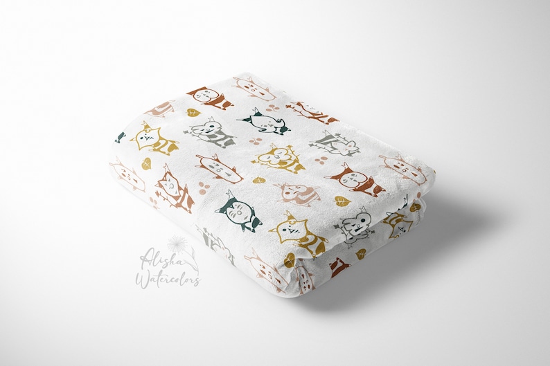 May include: A white fabric baby blanket with a repeating pattern of colorful cartoon cats. The cats are in various poses and have different facial expressions. The background is white with small brown and green dots.