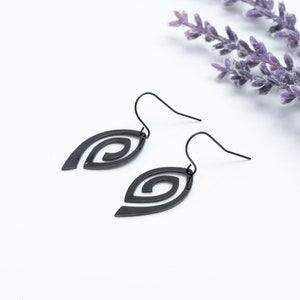 Puede incluir: Un par de pendientes negros colgantes con un diseño en espiral. Los pendientes están hechos de metal y tienen un aspecto simple y elegante.