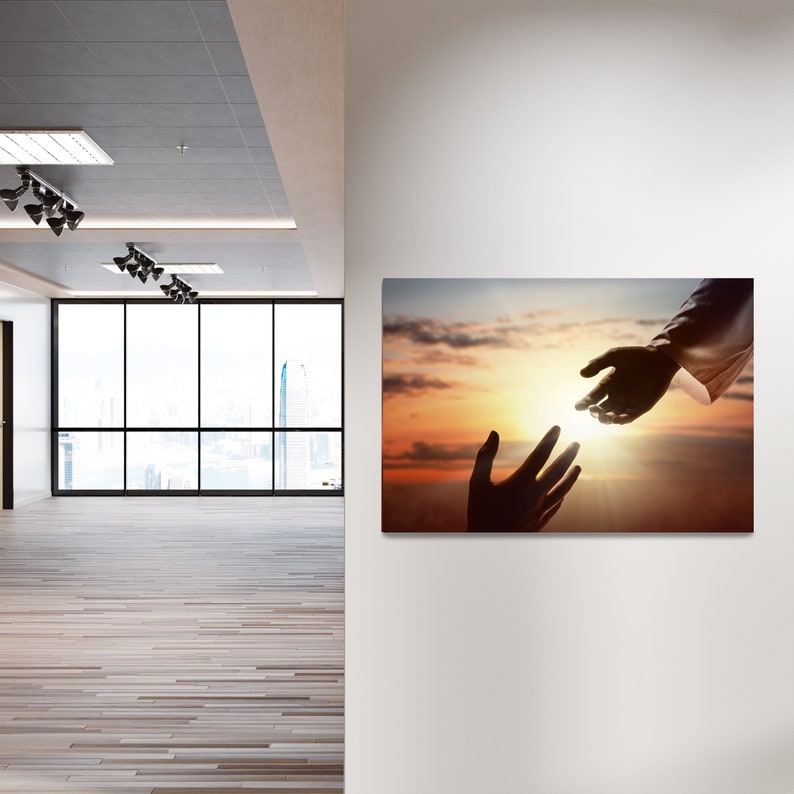 May include: A silhouette of two hands reaching towards each other against a sunset sky. The hand on the left is reaching up, while the hand on the right is reaching down. The sky is a mix of orange, pink, and purple.