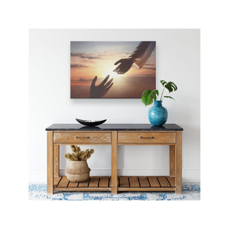 May include: A canvas print depicting a silhouette of two hands reaching towards each other against a sunset backdrop. The top hand is reaching down, while the bottom hand is reaching up. The image evokes a sense of hope and connection.
