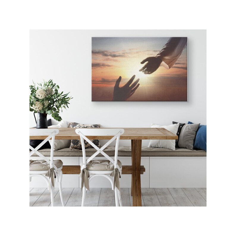 May include: A canvas print depicting a hand reaching out from a bright, cloudy sky towards another hand reaching up from the bottom of the image. The sky is a vibrant orange and yellow, with a bright light shining in the center.