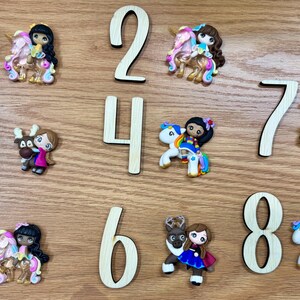 May include: A collection of eight numbered wooden digits arranged alongside eight distinct polymer clay figurines. The figures include characters riding unicorns, a character with a reindeer, and a character in a brown hat with a small animal.