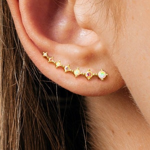 May include: Gold ear crawler with a row of small, iridescent opal stones. The crawler is curved and has a delicate design.