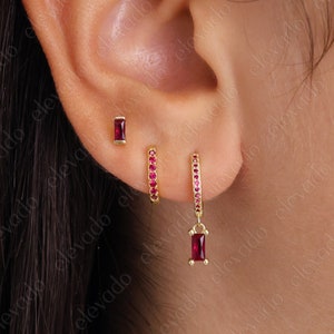 May include: A pair of gold earrings with red gemstones. The earrings are a small stud with a rectangular stone and a hoop earring with a dangling rectangular stone.