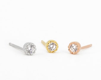 May include: Three stud earrings with a small round clear stone surrounded by a beaded halo. The earrings are shown in silver, gold, and rose gold.