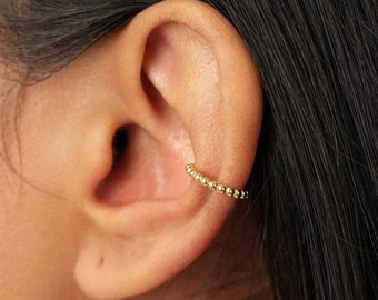 May include: A gold ear cuff with a beaded design. The cuff is worn on the upper part of the ear.