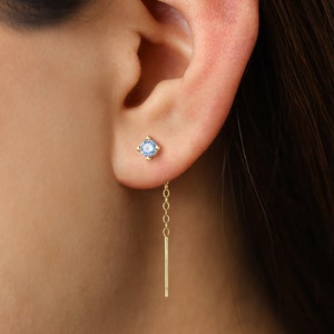 May include: Gold dangle earrings with a blue gemstone and a delicate chain.