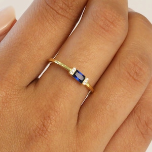 May include: A gold ring with a blue rectangular gemstone and small clear gemstones on either side.