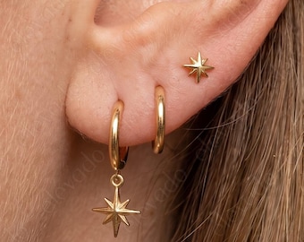 May include: A gold-toned ear jewelry set consisting of a small star-shaped stud earring, a plain gold hoop, and a gold hoop earring featuring a dangling star charm. The jewelry pieces are polished and have a metallic finish, worn in the earlobe.