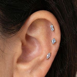 May include: A set of three ceramic mugs with a speckled, cream-colored glaze. Each mug features a different hand-painted floral design in shades of blue, green, and yellow. The mugs have a simple, rounded shape and a comfortable handle.