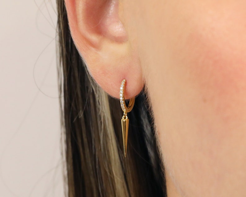 May include: Gold hoop earrings with a small diamond-encrusted band and a dangling gold spike.