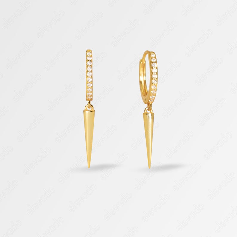 May include: Gold hoop earrings with a small, pointed spike dangling from each hoop. The hoops are lined with small, clear cubic zirconia stones.