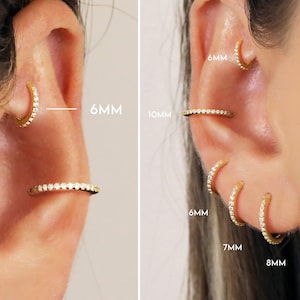 May include: Close-up of ears with gold-colored hoop earrings. The earrings are adorned with small, clear gemstones. The image shows different sizes: 6mm, 7mm, 8mm, and 10mm. The earrings are displayed on the ear.