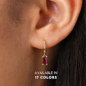 May include: A gold hoop earring with a rectangular, deep red gemstone pendant. The earring is shown on an ear. The text "AVAILABLE IN 17 COLORS" is at the bottom of the image.