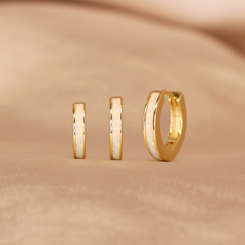May include: Set of three gold hoop earrings with a white opal inlay. The earrings are different sizes.