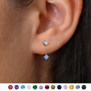 Peut inclure: Une paire de petites boucles d'oreilles en or avec une seule pierre précieuse bleu clair dans chacune. Les boucles d'oreilles sont présentées dans un gros plan d'une oreille.
