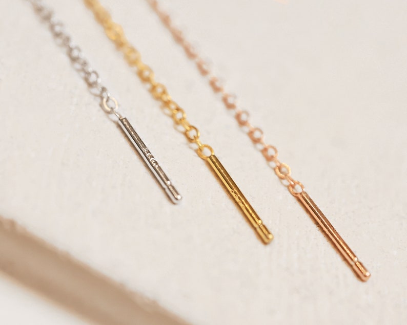 Puede incluir: Tres cadenas delicadas con puntas de metal de diferentes colores. Las cadenas son plateadas, doradas y de oro rosa.