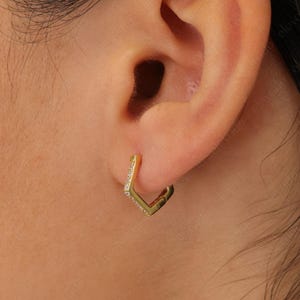 May include: Gold hoop earrings with a square shape and small clear stones.