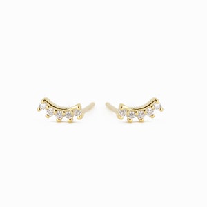 May include: A pair of gold earrings with a curved design and five small clear stones.